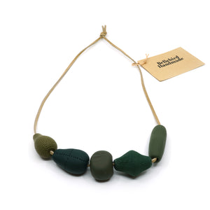Assorted green handmade beads threaded on light tan coloured suede cord.