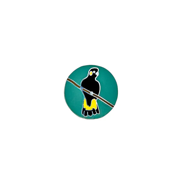 Enamel pin with a depiction of a yellow-tailed black cockatoo on a green background, designed by Tracy Colhoun.